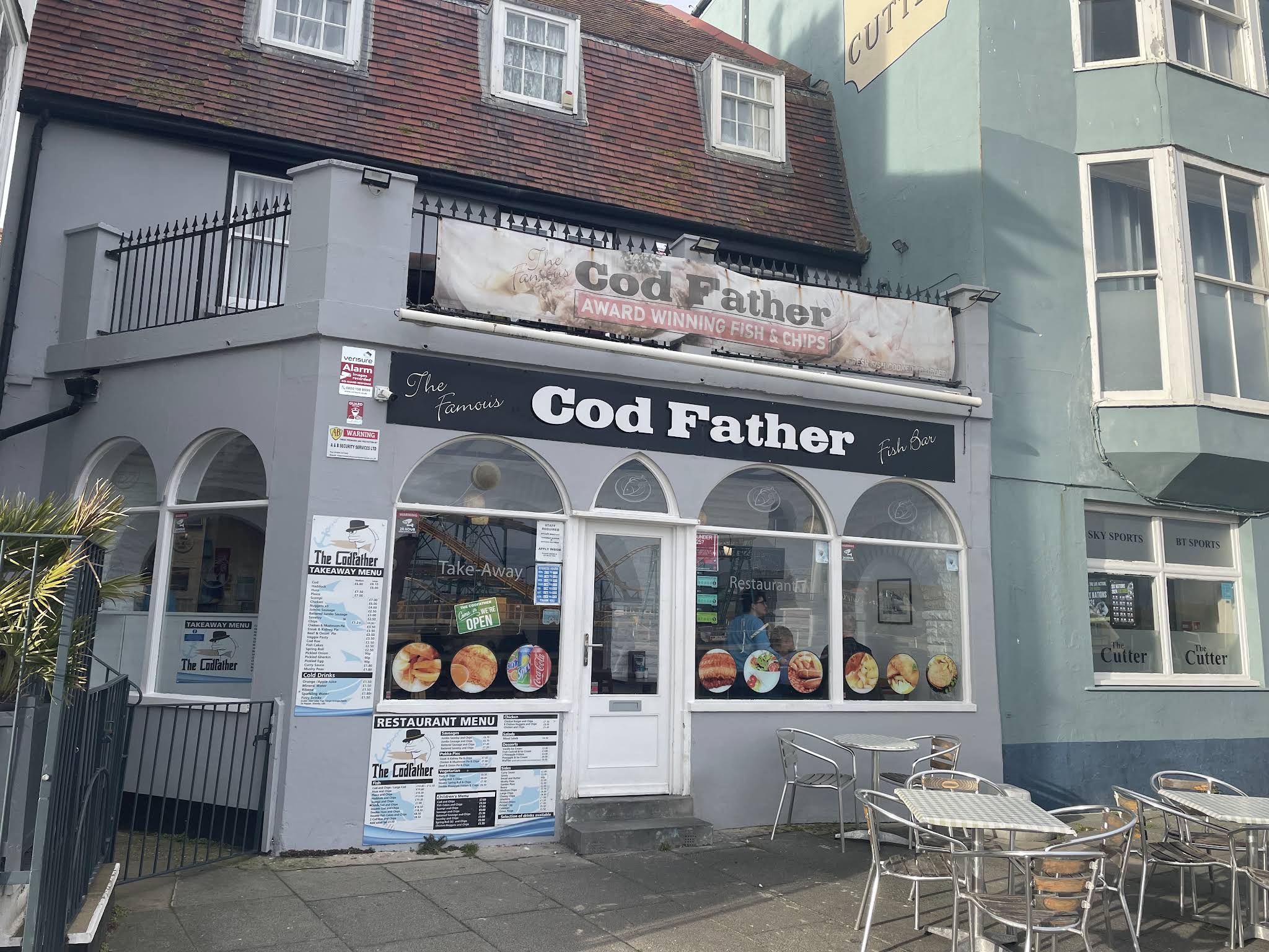 The complete Cod Father shopfront, with both signs, arched windows, entrance, threshold and outside tables visible