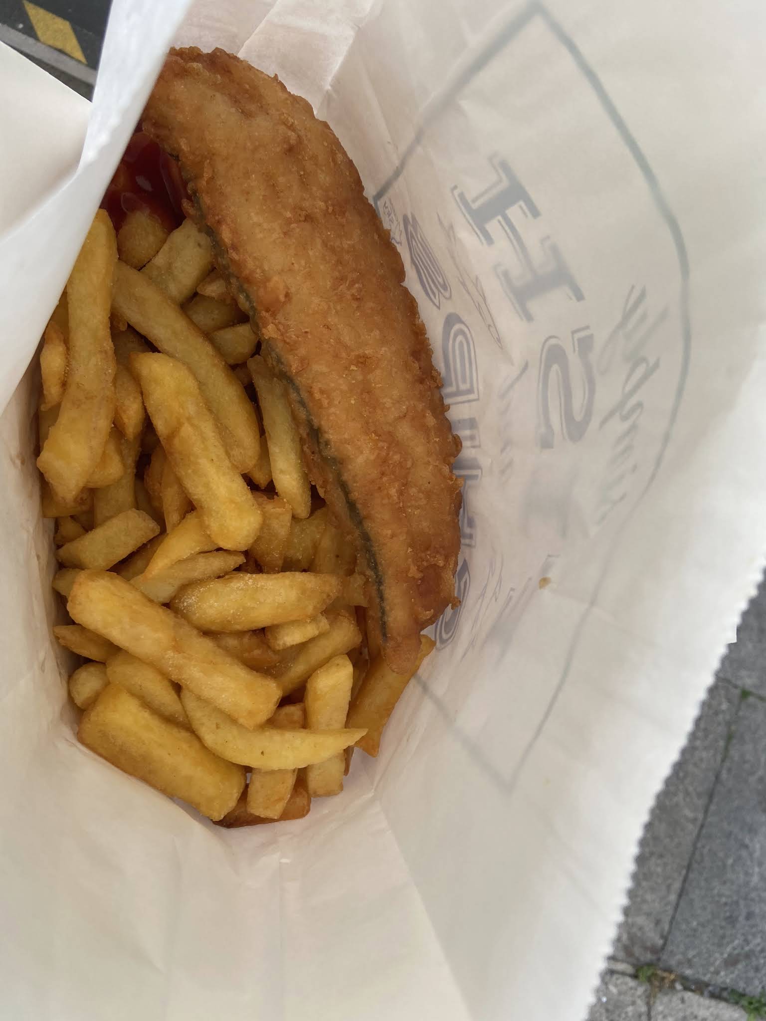 A whole golden battered fish and chips in takeaway paper at The Famous Cod Father